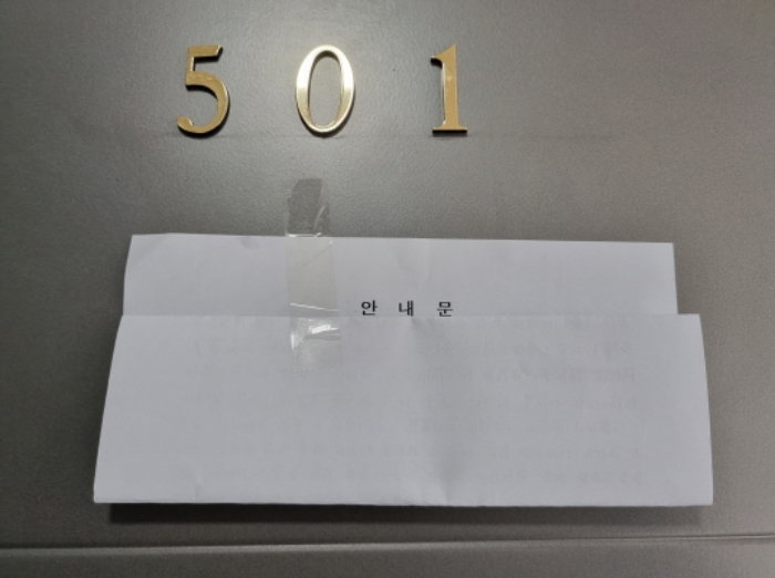 다세대주택 501호 현관문 — 금색 숫자 501 아래에 흰 봉투 형태의 '안내문'이 테이프로 붙어 있다.