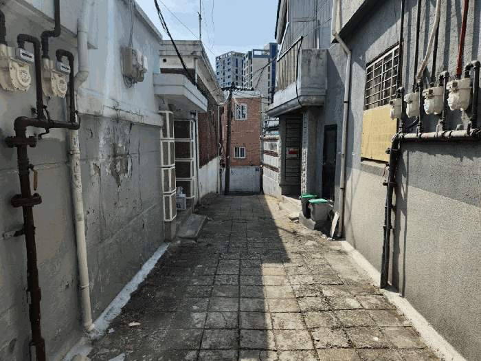 좁은 골목길 — 담과 담 사이 폭이 좁은 보행자 통로 형태의 길. 멀리 고층 아파트가 보인다.